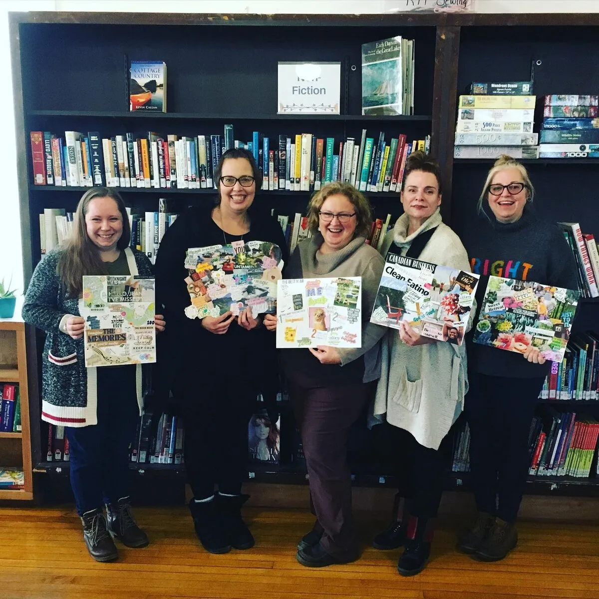 Five young women display their decorated scrapbook pages in a library in front of a bookshelf labeled "Fiction"